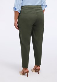 Pantaloni verdi a sigaretta con vita elastica, due tasche posteriori e una texture liscia, abbinati a sandali con tacco beige.