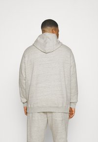 Haut de hoodie texturé gris clair avec une grande capuche et des poignets côtelés, vu de l'arrière. Présente une coupe décontractée et un design minimaliste.