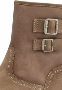 Braune Leder-Stiefelette mit zwei silbernen Schnallen, kontrastierendem weißen Stich und einer glatten Textur mit leichtem Glanz.