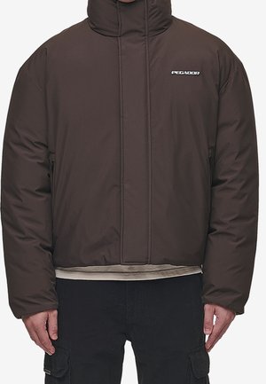 Homme portant une veste matelassée marron foncé avec col montant et poches latérales zippées, associée à un pantalon cargo noir.