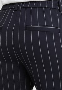 Granatowe spodnie w paski z białymi prążkami, z elastycznym pasem, dwoma tylnymi kieszeniami i gładką teksturą materiału.