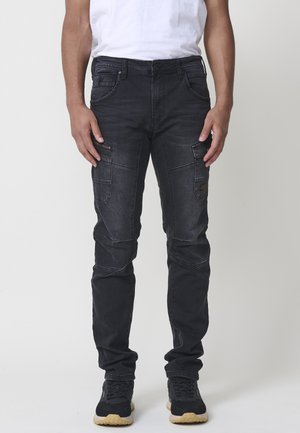 Jeans cargo negros con un corte slim, que cuentan con múltiples bolsillos, detalles de cremalleras y un ligero efecto desgastado. Fabricados en tela de mezclilla.