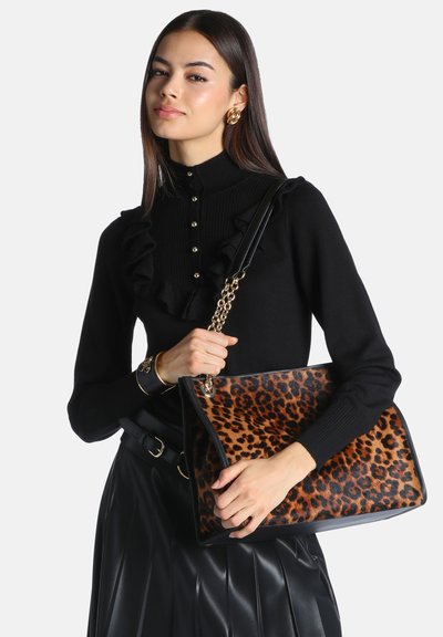 Femme portant un pull noir à volants et une jupe en cuir tenant un sac à main imprimé léopard avec une bandoulière chaîne dorée.