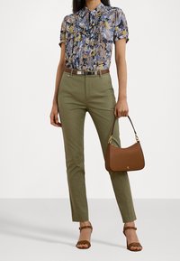 Blus med blommönster och volanger, olivgröna skräddarsydda byxor, brun läderhandväska och bruna sandaler med remmar.