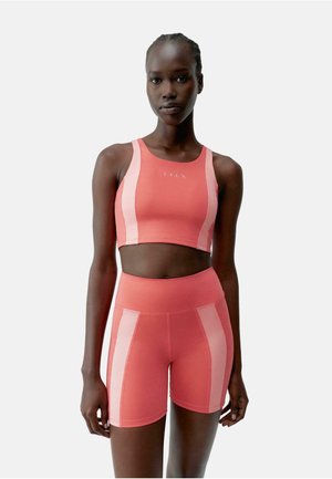 Koralfarvet sportsbh og shorts sæt med kontrasterende lyse paneler, tætsiddende design og glat tekstur. Ideelt til sportstøj.