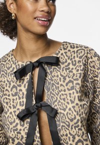 Top com padrão de leopardo, apresentando um decote redondo, laços de fita de seda preta e um tecido texturizado, com um recorte no peito.