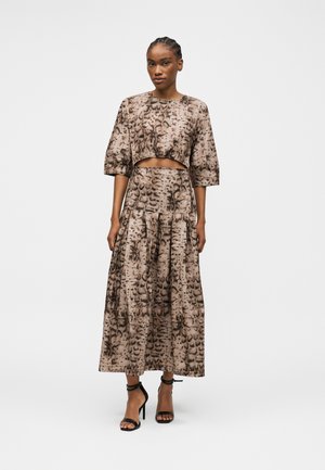 Mujer con el cabello trenzado que lleva un top corto de estampado animal en marrón y negro y una falda larga de talle alto a juego con tacones negros con correa en el tobillo.