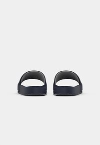 Egy pár sötétkék slip-on szandál egyetlen széles pánttal, elölről nézve, fehér háttér előtt.