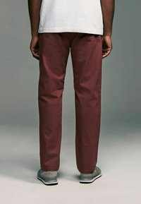 Pantalons bordeaux à coupe décontractée, en tissu lisse, associés à des baskets grises avec des accents en maille et des semelles noires.