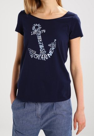 Kvinde iført navyblå T-shirt med et ankerdesign lavet af hvide ord, herunder create, smile, dream og love.