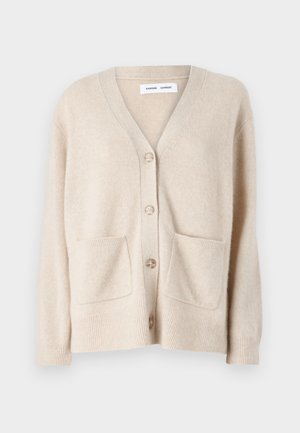 Beige Cardigan mit V-Ausschnitt, fünf Knöpfen, gerippten Bündchen und zwei Fronttaschen. Hergestellt aus weichem, texturiertem Stoff.
