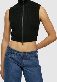 Svart ribbad ärmlös cropped top med högkrage och dragkedja, i kombination med blå denimjeans.
