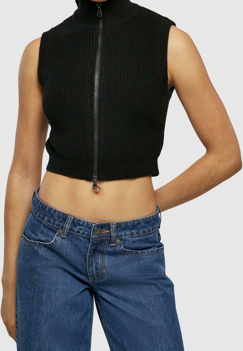 Svart ribbad ärmlös cropped top med högkrage och dragkedja, i kombination med blå denimjeans.
