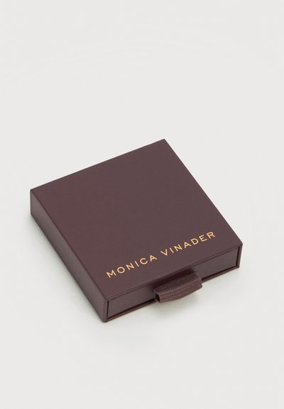 Σκούρο καφέ τετράγωνο κουτί κοσμημάτων με υφασμάτινη θηλιά τράβηγμα, με χρυσοτυπία "Monica Vinader" στο καπάκι.