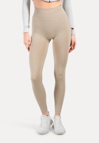 Leggings beige a vita alta, realizzati in tessuto elastico, con una texture liscia e un design aderente, abbinati a scarpe da ginnastica bianche.