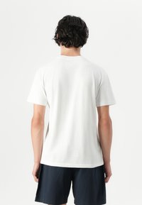 Tricou alb din bumbac, cu mâneci scurte, guler rotund și o croială lejeră, asociat cu pantaloni scurți bleumarin. Design simplu, fără modele vizibile.
