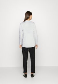 Witte lange mouwen shirt met een gebogen zoom en knoopmanchetten, gecombineerd met zwarte op maat gemaakte broeken en zwarte oxford schoenen.