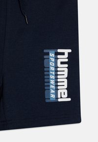 Pantalones cortos azul marino con una textura suave que presentan un logo en blanco y azul claro de "Hummel Sportswear" en el lateral. Incluyen un cordón ajustable.