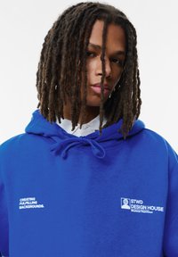 Felpa blu con cappuccio dotata di lacci regolabili, tasca frontale e testo bianco. Logo e slogan sul petto. Tessuto morbido.