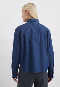 Dunkelblaue Jeanshemd mit Kragen, langen Ärmeln und geknöpften Manschetten. Hat einen lässigen Schnitt und sichtbare Nähdetails.