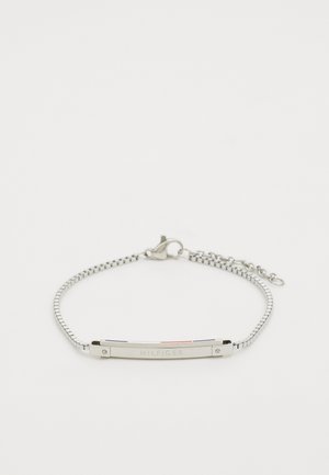 Bracelet en métal argenté avec un centre plat orné d'accents rouge, blanc et bleu. Les maillons de la chaîne permettent un ajustement facile. Nom de la marque gravé.