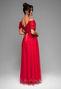Robe de soirée rouge avec un design décolleté, des manches bouffantes, un ruban noué à la taille et une jupe fluide et transparente. Texture lisse.