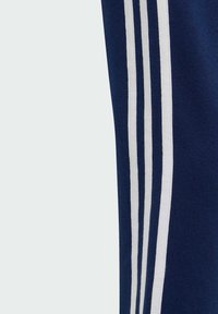 Marineblaue Sporthose mit drei vertikalen weißen Streifen an der Seite, aus einem weichen, strukturierten Stoff.