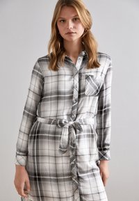 Juodai-baltas šiltas plaid marškinių suknelė, pagaminta iš minkštos medžiagos. Yra mygtukų uždarymas, ilgomis rankovėmis, juosmens juosta ir krūtinės kišenė.