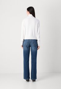 Hvit strikket genser med høy krage, kombinert med blå vide jeans. Outfiten har ribbede mansjetter og en avslappet passform i stoffet.