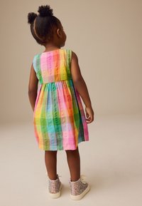 Kolorowa, bezrękawnikowa sukienka z marszczonym stanem, z pionowymi paskami w kolorach różowym, zielonym, żółtym i niebieskim. Błyszczące, wysokie trampki.