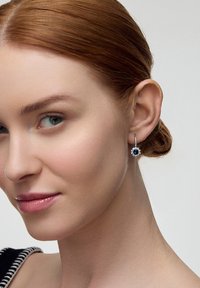 Srebrne kolczyki w kształcie kropli z niebieskim szafirem i kwiatowym wzorem, z centralnym głęboko niebieskim kamieniem otoczonym białymi akcentami.