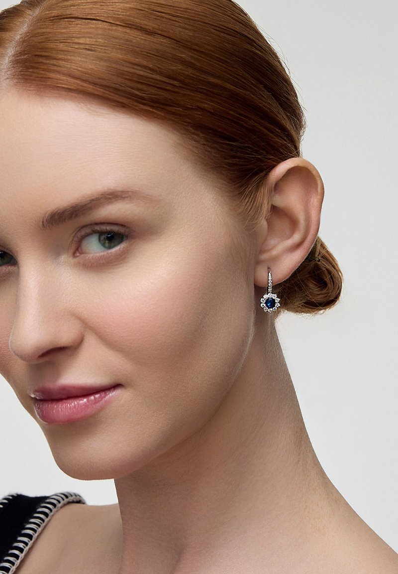 Srebrne kolczyki w kształcie kropli z niebieskim szafirem i kwiatowym wzorem, z centralnym głęboko niebieskim kamieniem otoczonym białymi akcentami.