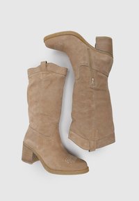 Botas de ante de color tostado hasta la rodilla, con parte superior texturizada, cremallera lateral y tacón cuadrado. Presentan sutiles detalles de costura cerca del dedo del pie.