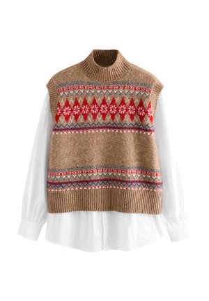 Stickad ärmlös tröja i beige med röda, blå och vita geometriska mönster. Har en ribbad halsringning och nederkant, lagd över en vit skjorta med krage.