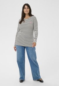 Bluză cu mâneci lungi cu dungi alb-negru din bumbac, având un mic accent în formă de inimă roz. Asortată cu blugi evazați din denim albastru.