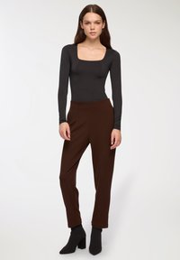 Czarny bodysuit z długim rękawem i kwadratowym dekoltem, w połączeniu z brązowymi spodniami o zwężanym kroju oraz czarnymi botkami na obcasie. Gładka tekstura materiału.