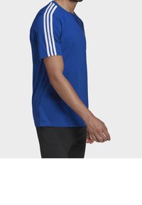 Blå t-shirt med kort ärm, som har tre vita ränder på varje axel och rundad halsringning. Tillverkad av mjukt bomullstyg.