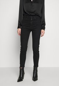 Černé skinny džíny s vysokým pasem, zapínáním na knoflík a rozptýlenými kamínky. V kombinaci s černou saténovou blůzou a kotníkovými botami.