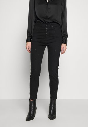 Jeans negros ajustados con una cintura alta, cierre de botón y embellishments de rhinestone dispersos. Combinados con una blusa de satén negra y botas de tobillo.