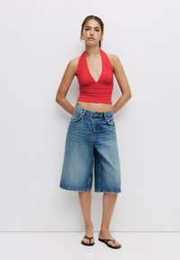 Crvena halter crop majica u kombinaciji s svijetlosivim traper šortsevima, koji prikazuju opušteni kroj. Model nosi crne japanke, uz minimalne dodatke.