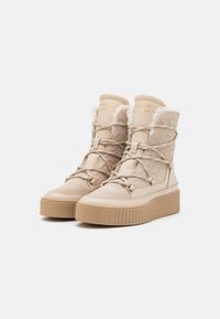 Beige snestøvler med en textureret overdel, pelskrave og tykke gummisåler. Har sporty snørebånd og metal accenter.