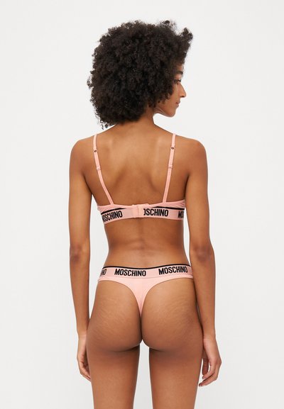 Rozā veļa komplekts ar melnu logotipa jostu, minimālistisks dizains, regulējami siksniņas un bezšuvju konstrukcija ērtībai.