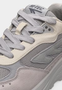 Sivo-bež Hi-Tec tenisica s mrežastim i brušenim panelima, podstavljenim jezičkom i debelim jastučićem na potplatu, vezana ravnim sivim vezicama.