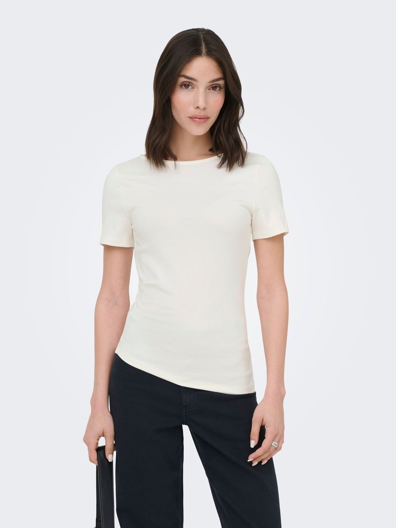 Femme aux cheveux foncés mi-longs, portant un haut blanc moulant à manches courtes et un pantalon noir, tenant un sac noir d'une main.