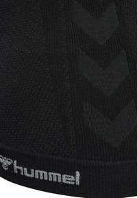 Close-up van zwart stof met getextureerde chevronpatronen en wit "hummel" logo gebreid langs de rand.