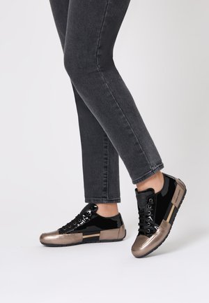 Black and metallic bronze sneakers with a glossy patent finish, featuring a rounded toe, lace-up closure, and textured rubber sole.