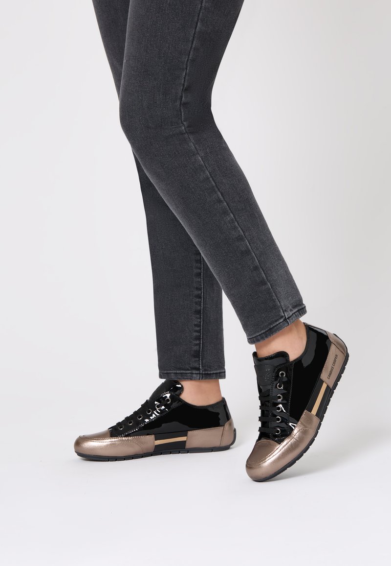 Zapatillas negras y de bronce metálico con un acabado brillante de charol, presentan una punta redonda, cierre de cordones y una suela de goma texturizada.
