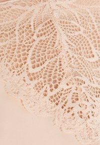 Pfirsichfarbener Spitzenstoff mit filigranen floralen Mustern, ausgestattet mit einem gewellten Rand und feinen Details, über einem glatten, einfarbigen Untergrund geschichtet.