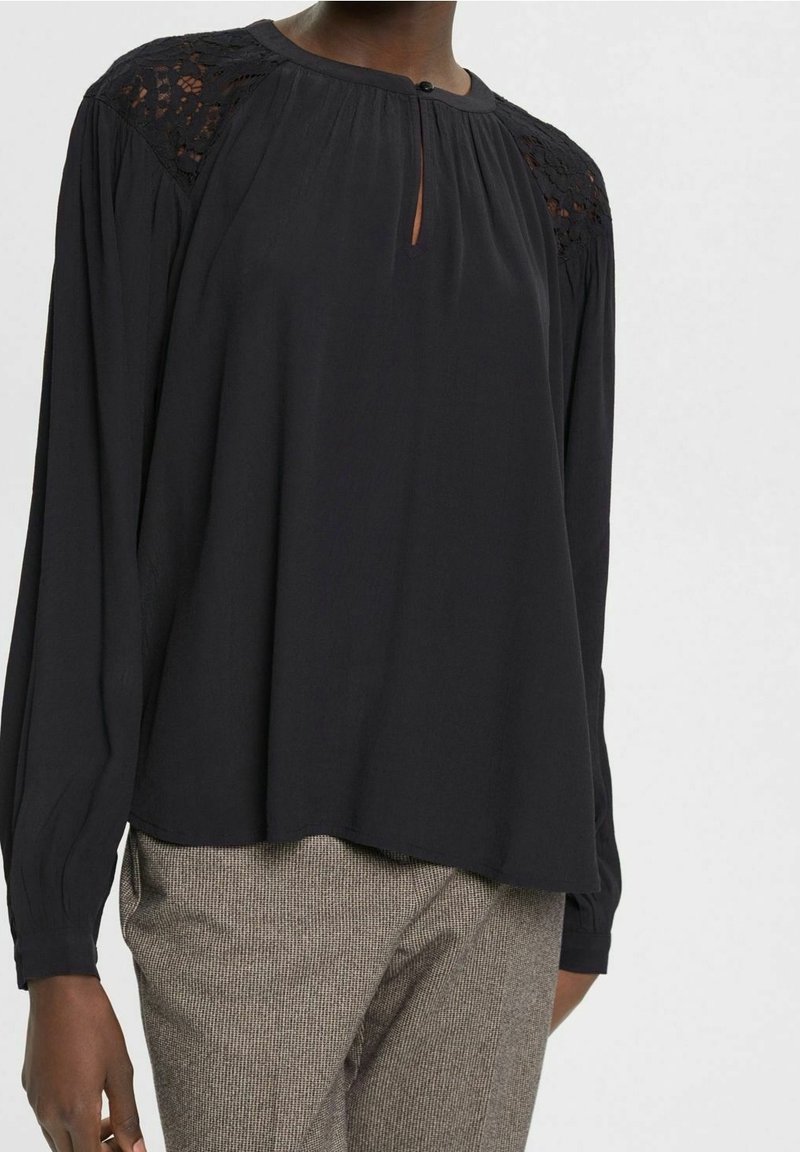 Sort langærmet bluse med rund halsudskæring, prydet med blonde detaljer på skuldrene og en nøglehulåbning foran. Blødt stof.