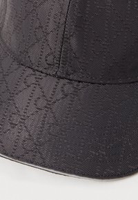 Fekete sapka texturált anyagból, finom mintával. A design ívelt napellenzőt és merev fejpántot tartalmaz.